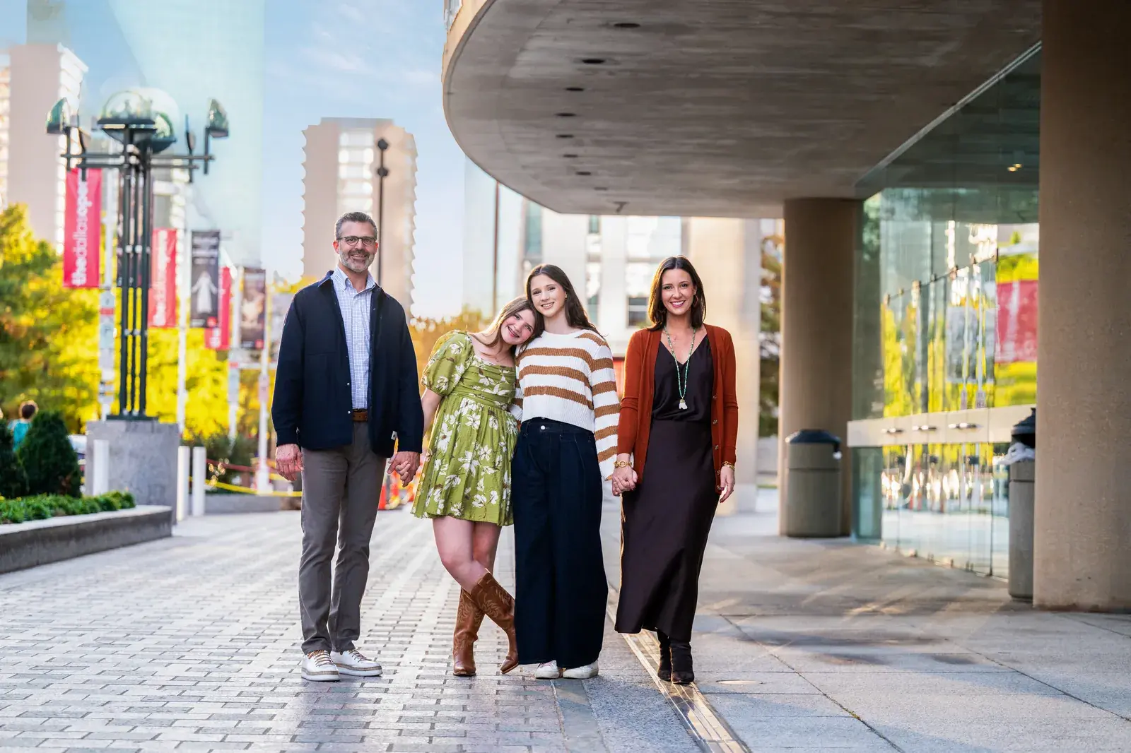 Family of four walking hand in hand on a downtown plaza at golden hour